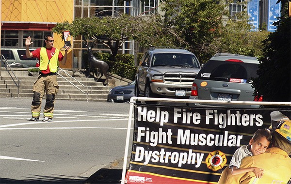 Eastside Fire & Rescue firefighter Paul Stevens waves at oncoming traffic while holding up a boot at the corner of Northeast Eighth Street and 228th Avenue Northeast in Sammamish June 26.